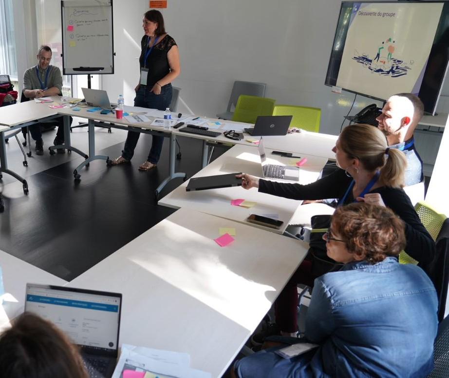 Photo d'illustration : une dizaine de personnes sont assises autour de tables disposées en carré et participent à un atelier.
