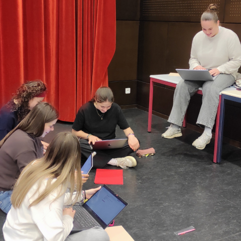 Photo décorative : un groupe de cinq étudiantes travaillent assises par terre et sur une table, dans un amphithéâtre.