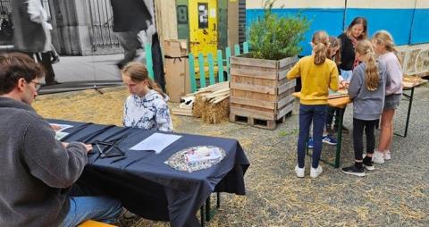 Photo d’Axel Ropert aidant une petite fille à assembler les barres d’un dôme géodésique en plastique. A l’arrière-plan, un groupe d’enfants autour d’une table et participant à l’atelier.