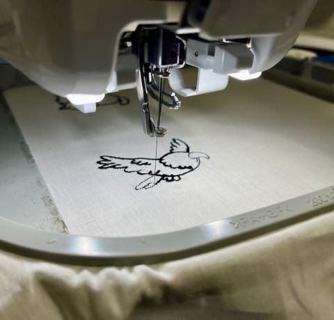 Photo en gros plan de la brodeuse numérique de l'Edulab en train de réaliser un motif de perroquet avec du fil noir, sur un tissu beige.