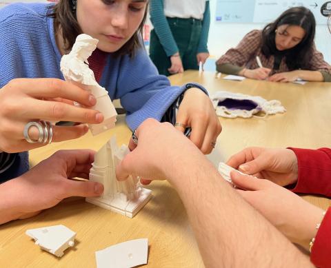 Photo de trois personnes en train d'assembler différents éléments en plastique blanc, imprimés en 3D, afin de constituer une statuette de déesse grecque d'une vingtaine de centimètres de haut.