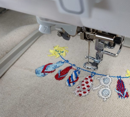 Photo d'une broderie réalisée avec la machine de l'Edulab : des tongs de différentes couleurs accrochées à un fil à linge, tenu par un soleil