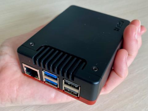Photo de la Supbox tenue dans une main. Il s'agit d'un petit boîtier d'une dizaine de centimètres comportant des prises réseaux et des ports USB.