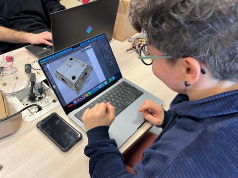 Photo d'une personne assise devant son ordinateur et travaillant à la conception d'un outil en contreplaqué de 15 cm sur 20 cm.